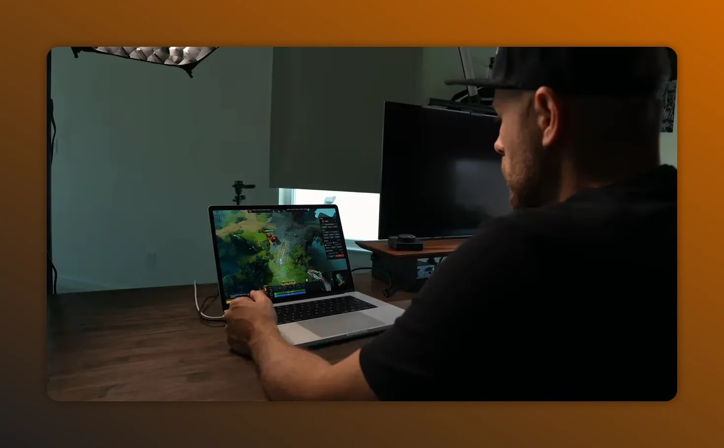 Man playing a game on a laptop while seated at a desk with additional displays