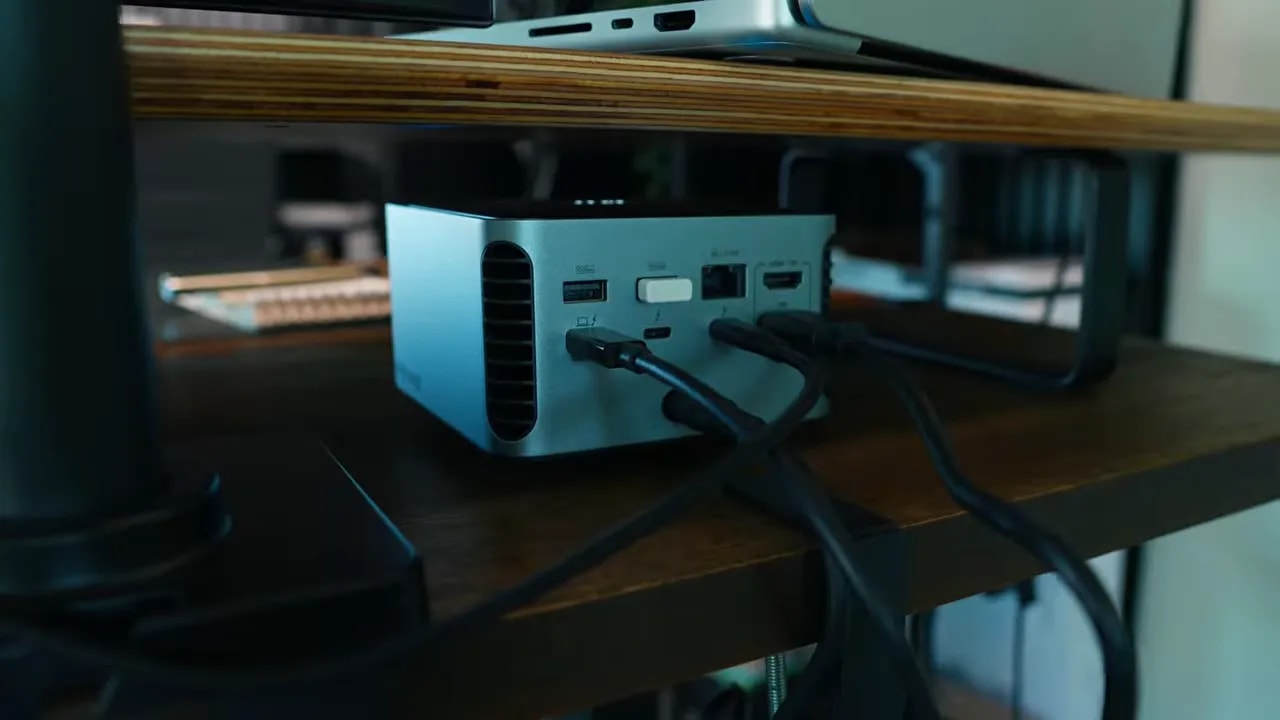Anker dock beneath a wooden desk shelf with several cables connected at the rear