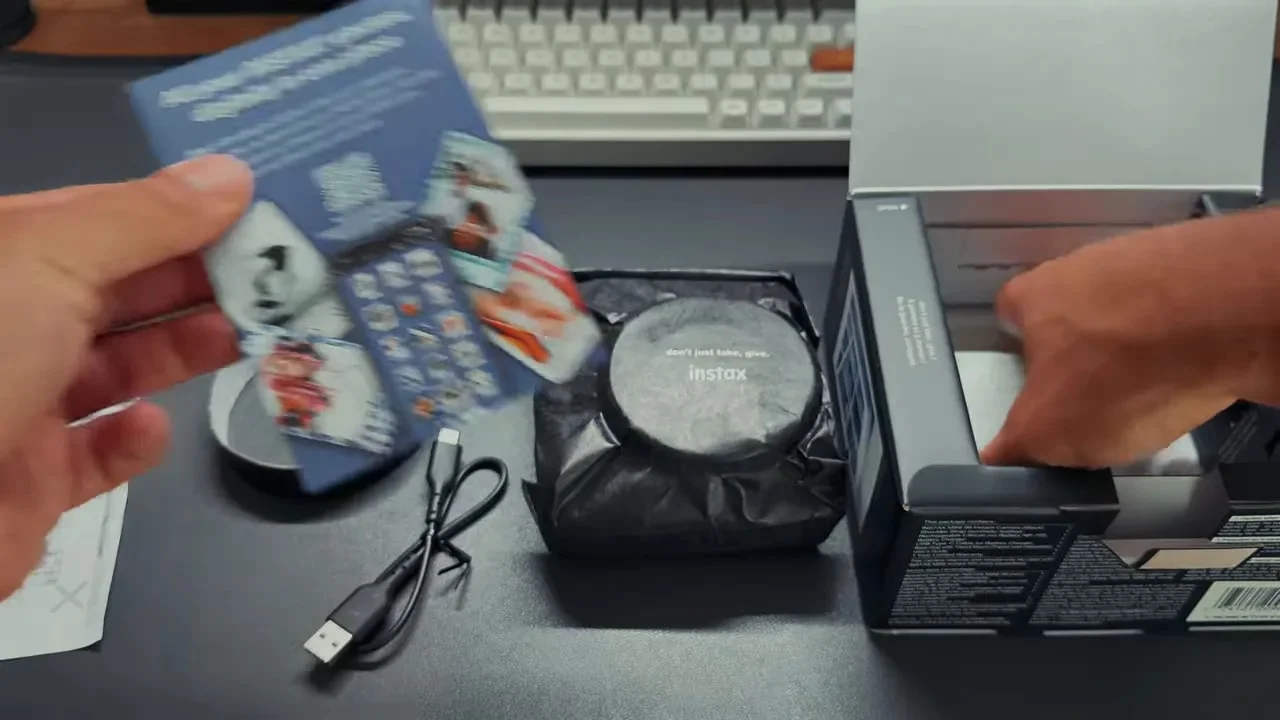 Opened box with camera wrapped in black pouch, cable, papers, and accessories laid out on desk