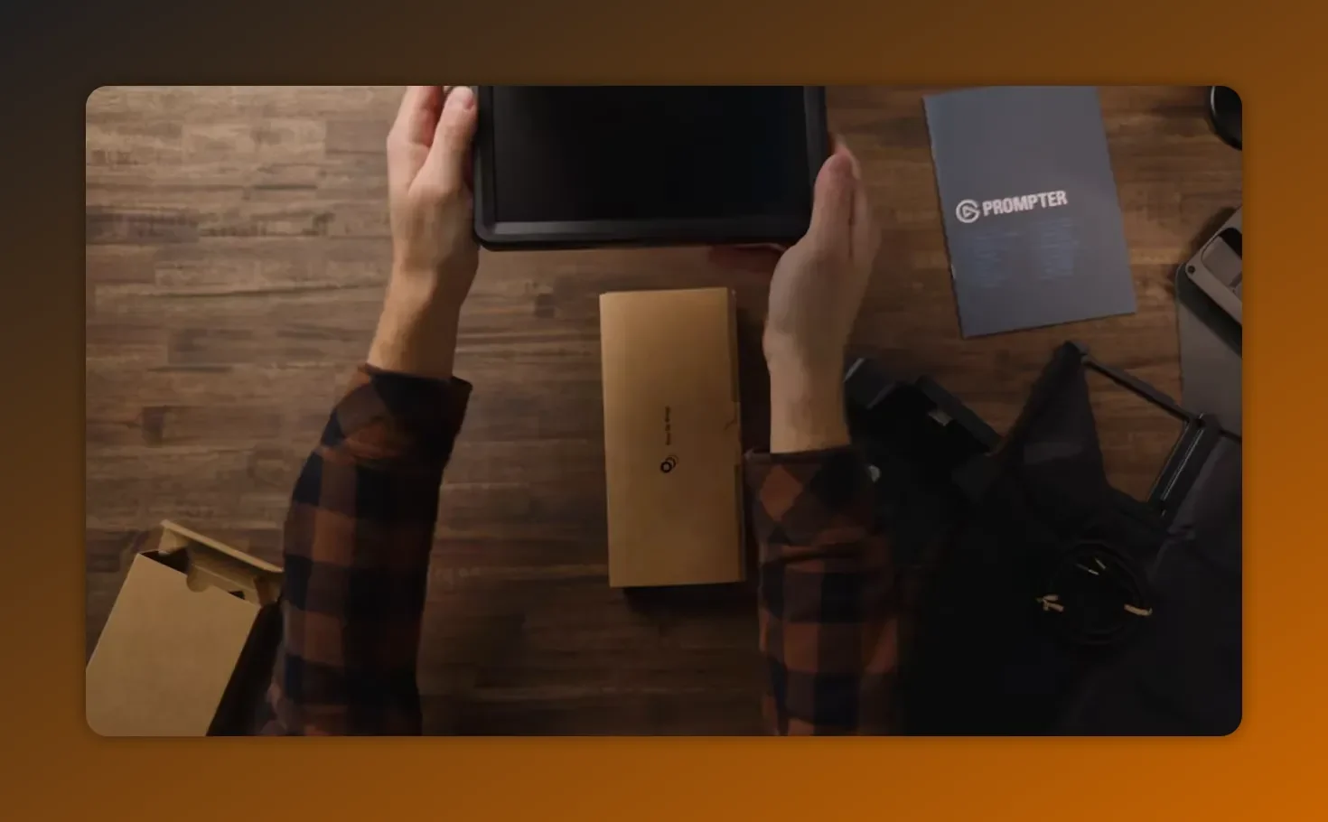 Top down shot of the elgato prompter 9 inch display held above its box with the manual visible on the table.