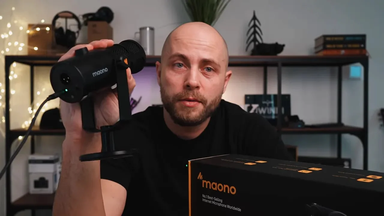 Reviewer holding a Maono PD200W box during an unboxing, with part of the setup visible
