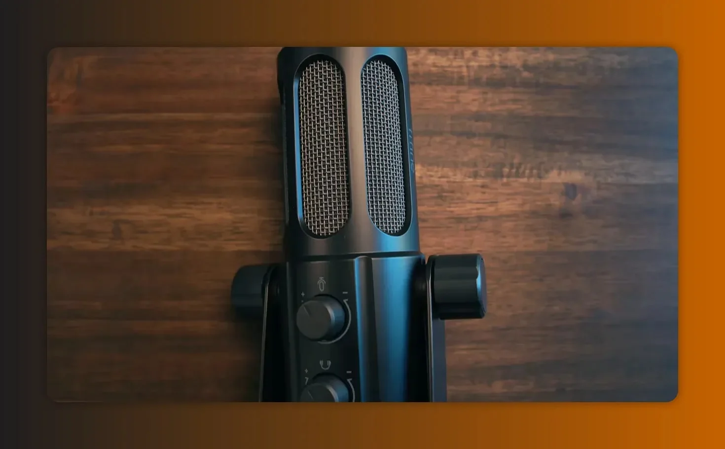 Top-down close-up of a Fifine Tank 6 microphone showing the metal grille and two control knobs on a wooden surface.